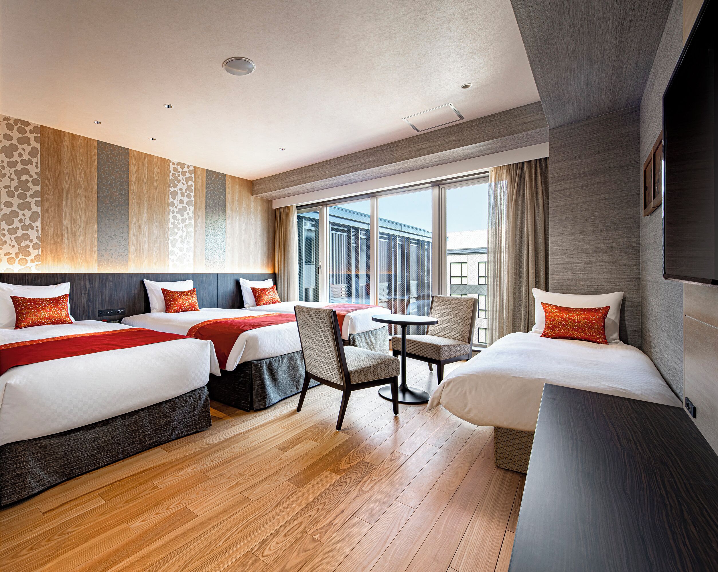 A hotel room with three beds, a small table, and a chair.