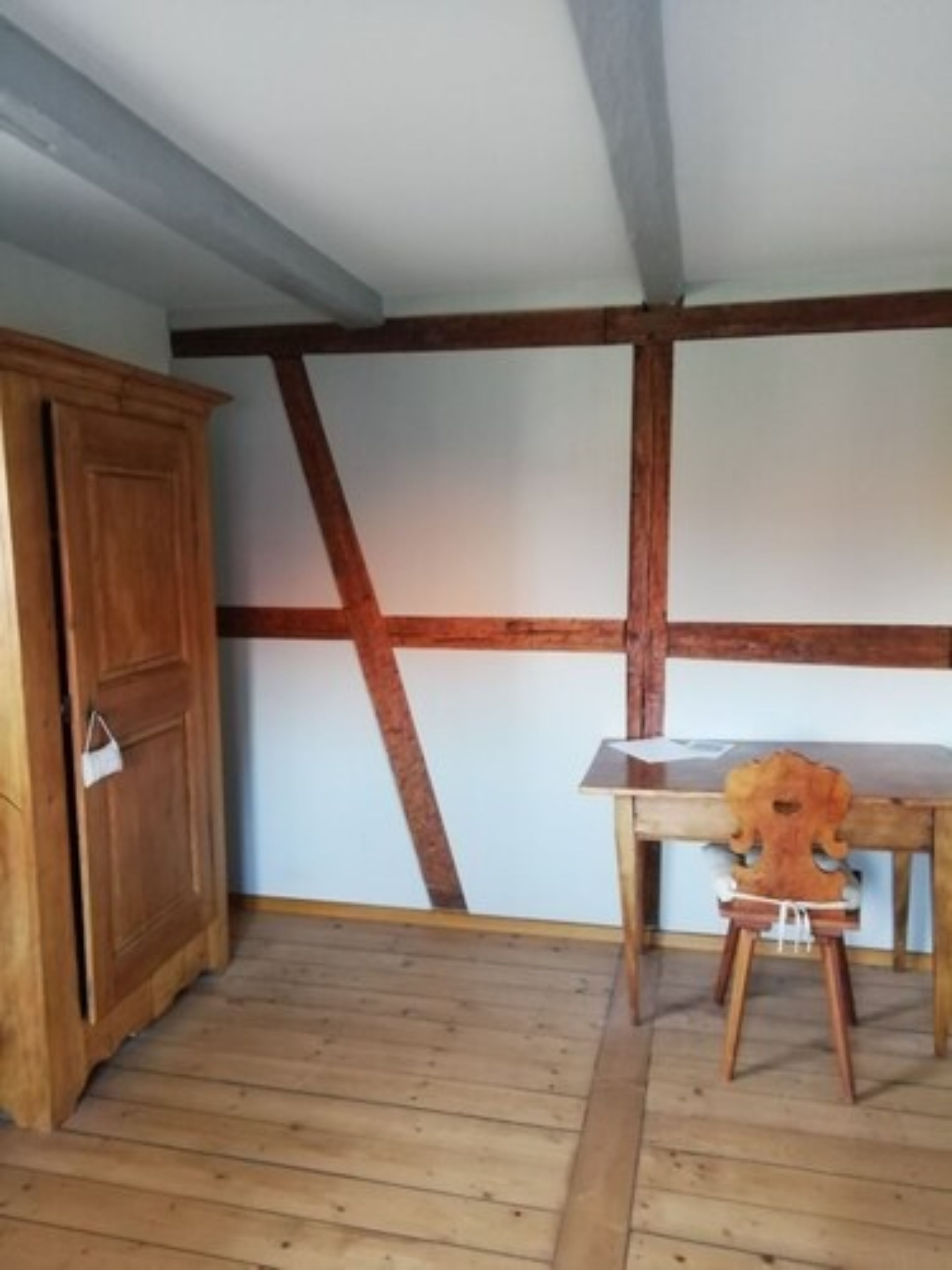 A room with exposed wooden beams, a wooden cabinet, and a table with a chair.
