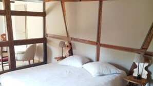 A bedroom with a large bed, wooden beams, a small table with a lamp, and a chair.