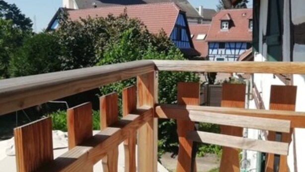 A wooden deck with a cushioned bench and a view of a church tower and traditional buildings in the background.