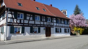 A traditional half-timbered building with a red tiled roof, multiple windows, and a visible door.