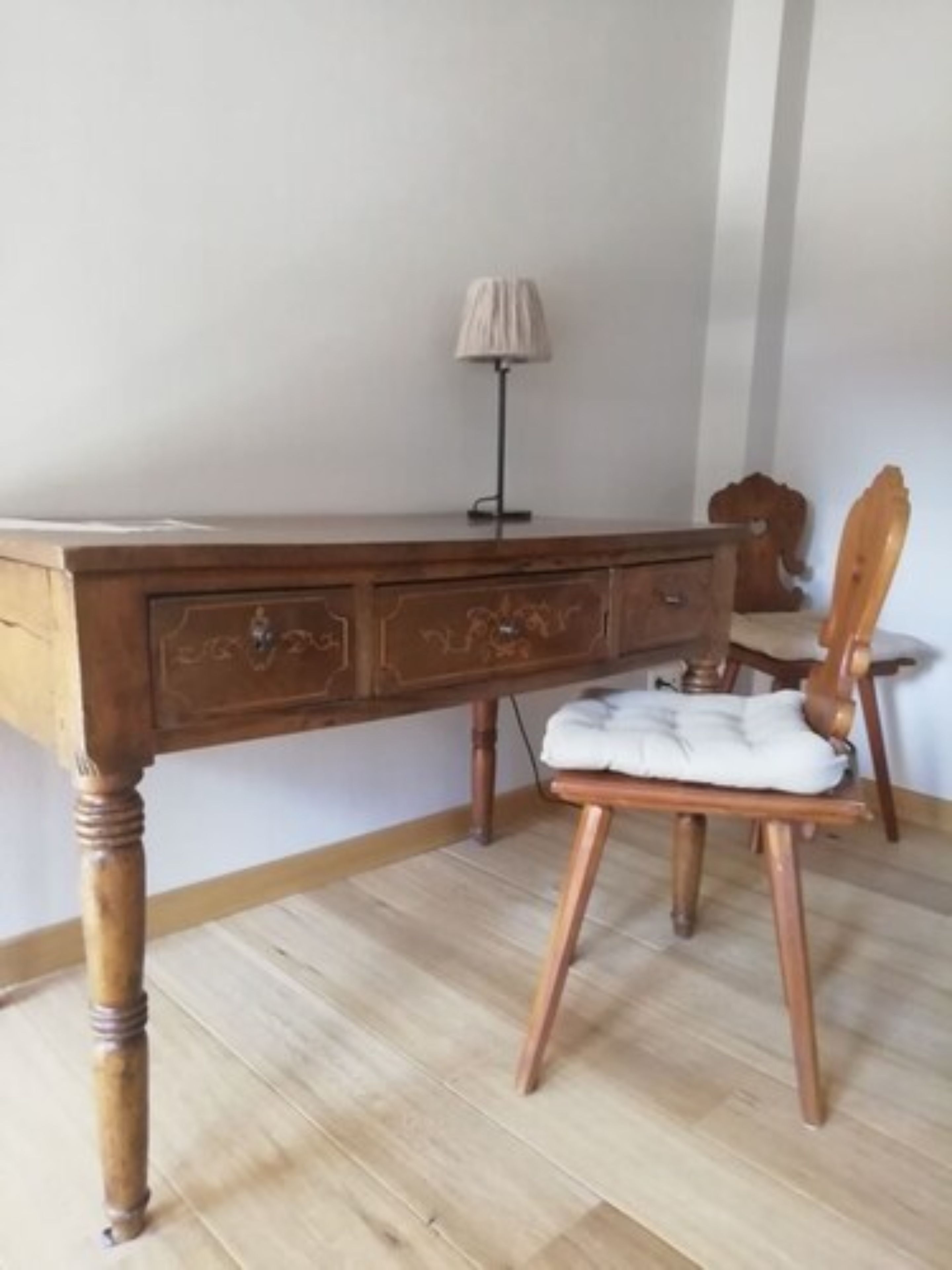 Ein Holztisch mit Schubladen, einer Lampe und einem Stuhl mit Sitzkissen.