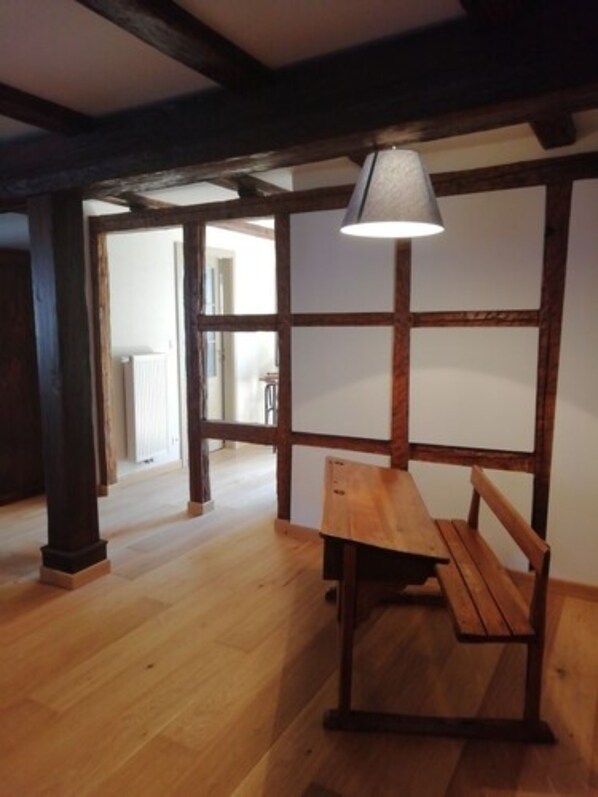 Una habitación con suelo de madera, un banco y una lámpara.