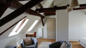 A cozy attic bedroom with a sloped ceiling, two windows, a bed, a chair, and a small table.