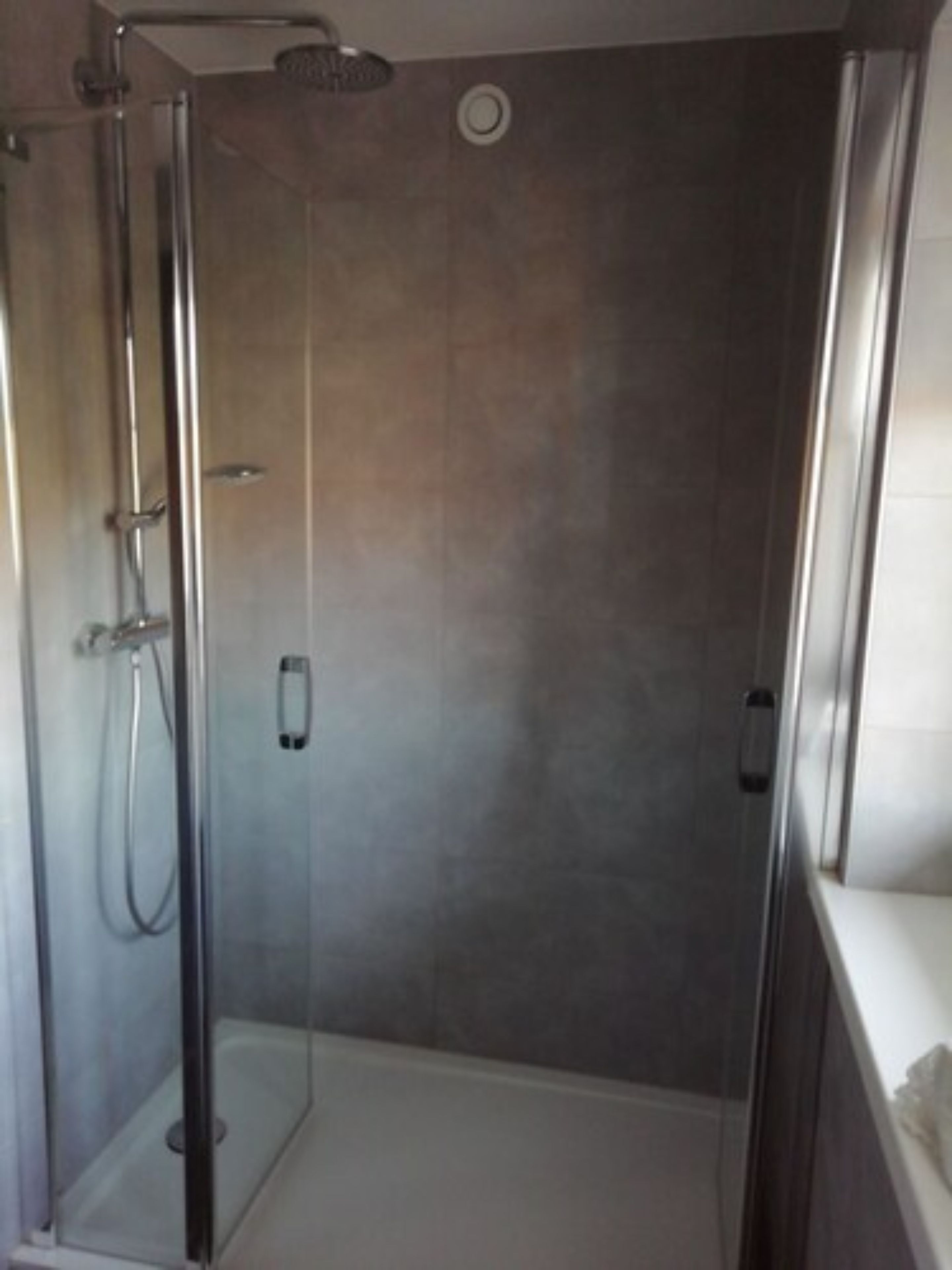 Una zona de ducha con paredes de vidrio, un panel de control y un cabezal de ducha de mano.