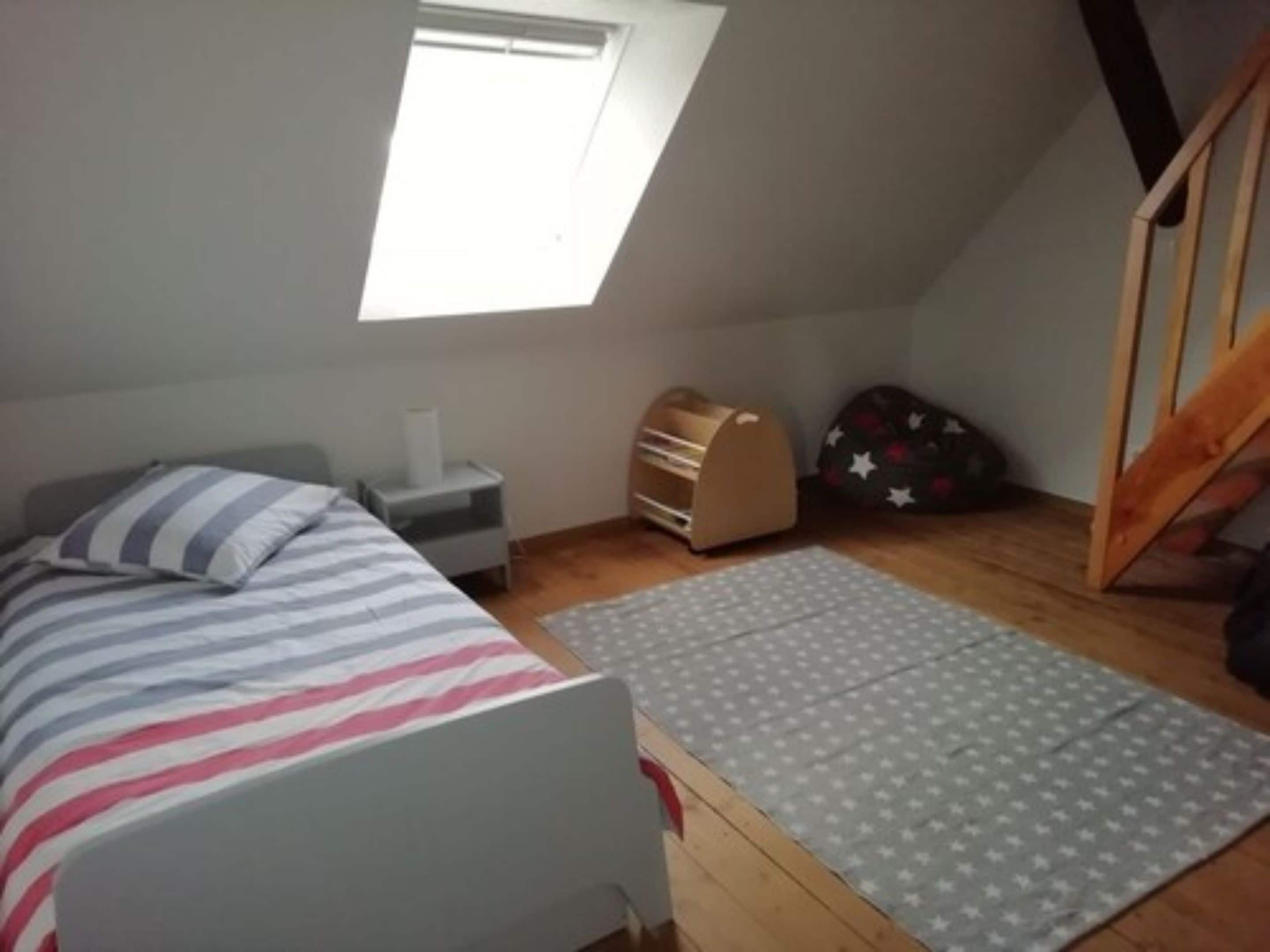 A small, sloped room with a bed, a nightstand, a desk, a chair, and a window.
