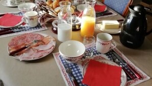 A breakfast table set with plates, cups, and a coffee pot in a room with a window, a sofa, and a lamp.