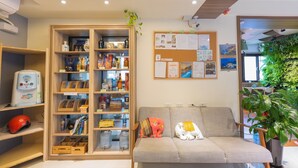 A modern room with a sofa, a wooden cabinet with various items, a bulletin board with papers, and a potted plant. - Mayu Hotel (Nangan)