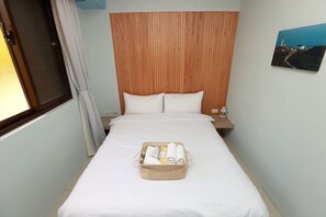 A neatly made bed with a wooden headboard, a bedside table with a lamp, and a wall-mounted painting. - Mayu Hotel (Nangan)