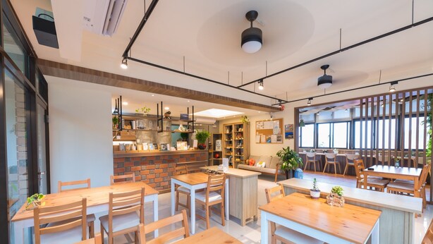 A modern cafe with wooden tables and chairs, a brick counter, and large windows. - Mayu Hotel (Nangan)