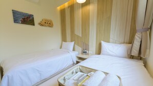 A hotel room with two beds, a bedside table with a bottle and a glass, and a wall-mounted picture of deer. - Mayu Hotel (Nangan)