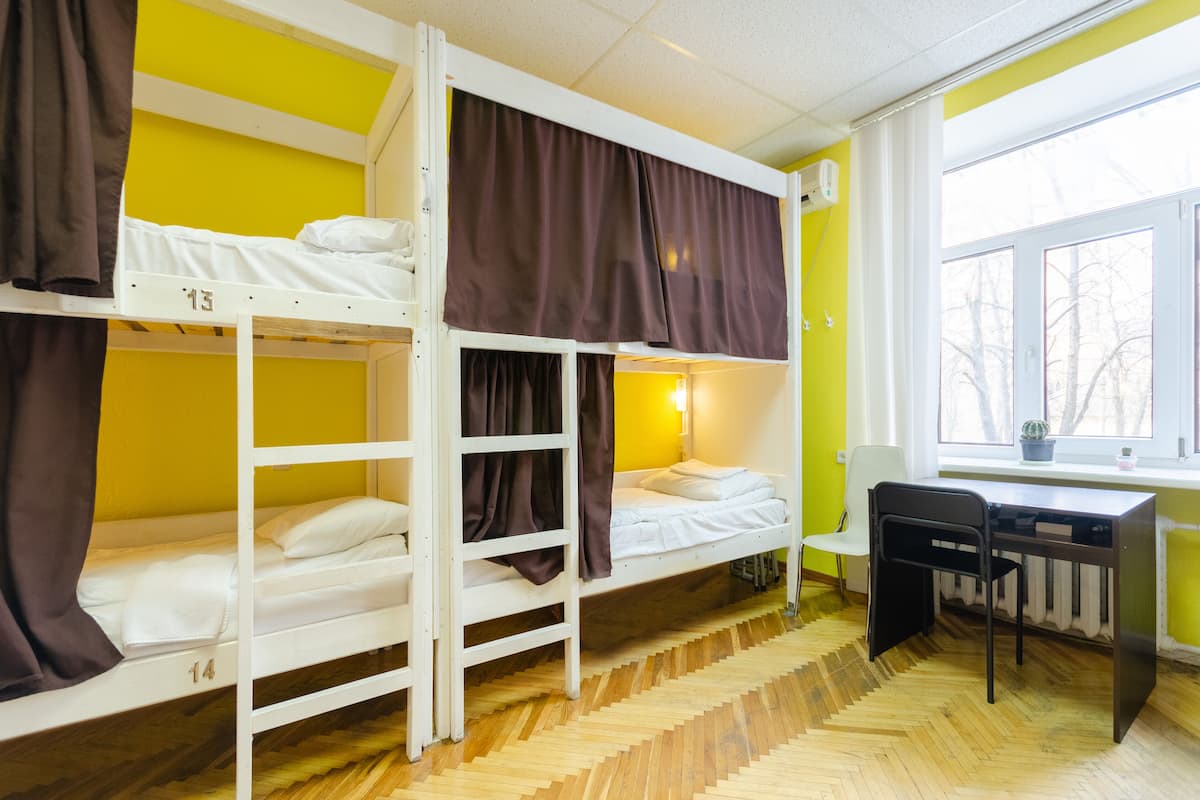 Quarto de dormitório com beliches, uma mesa e uma janela com vista para árvores.
