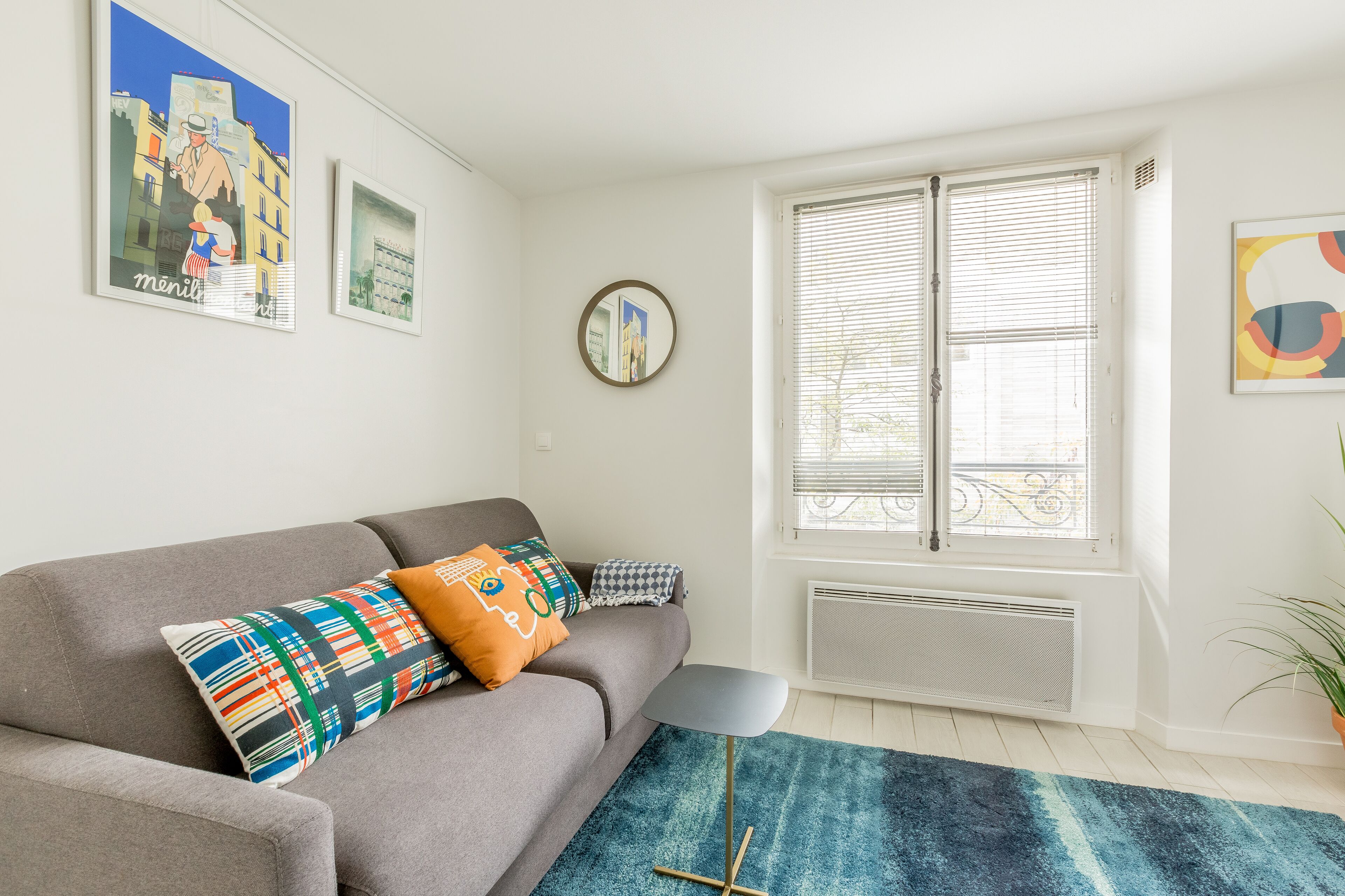 A modern living room with a grey sofa, colorful cushions, a blue rug, and artwork on the walls.