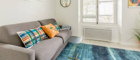 A modern living room with a grey sofa, colorful cushions, a blue rug, and artwork on the walls.