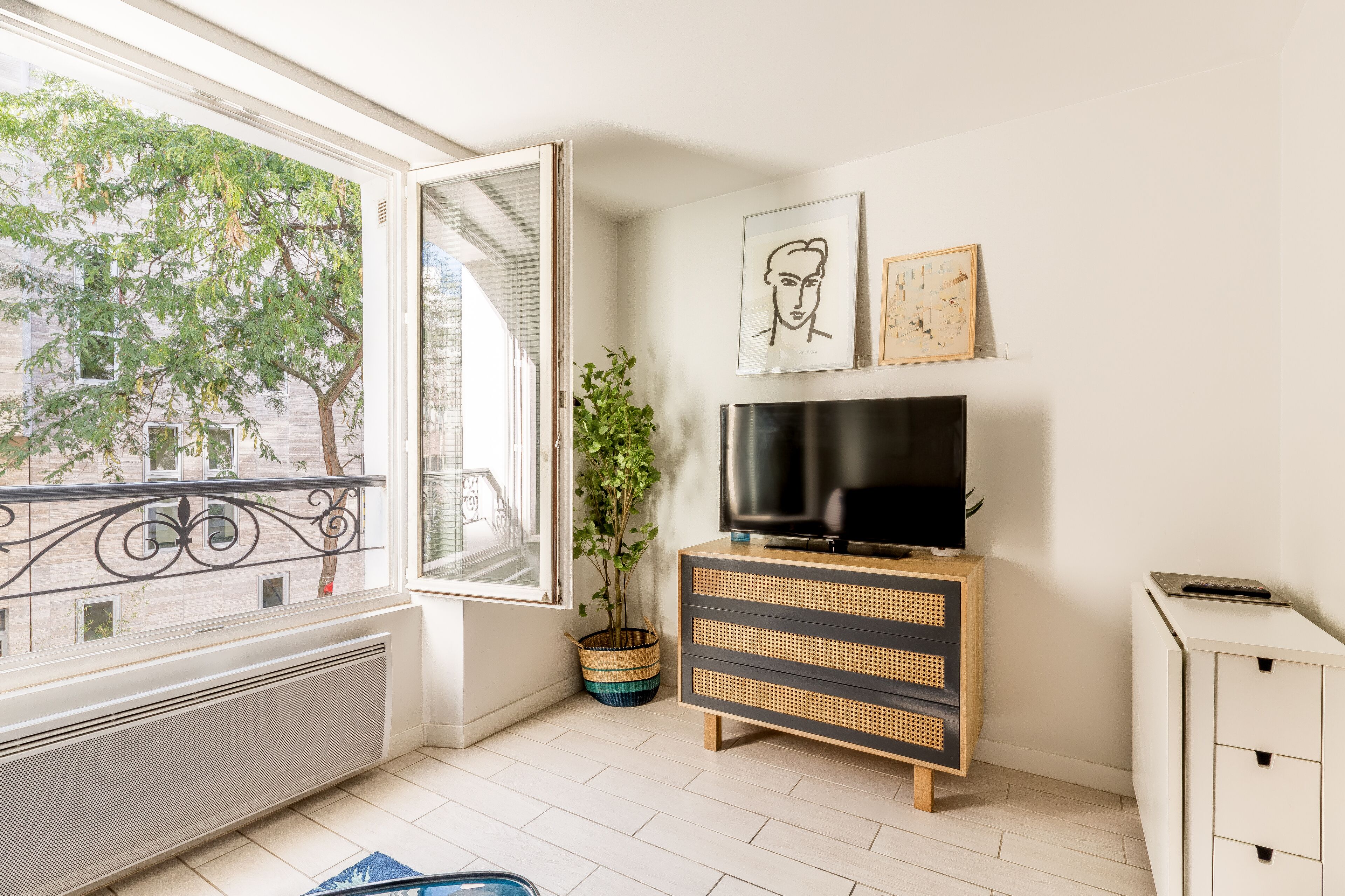 Ein modernes Wohnzimmer mit Fernseher auf einem Holzschrank, einem Blumentopf und Kunstwerken an der Wand.