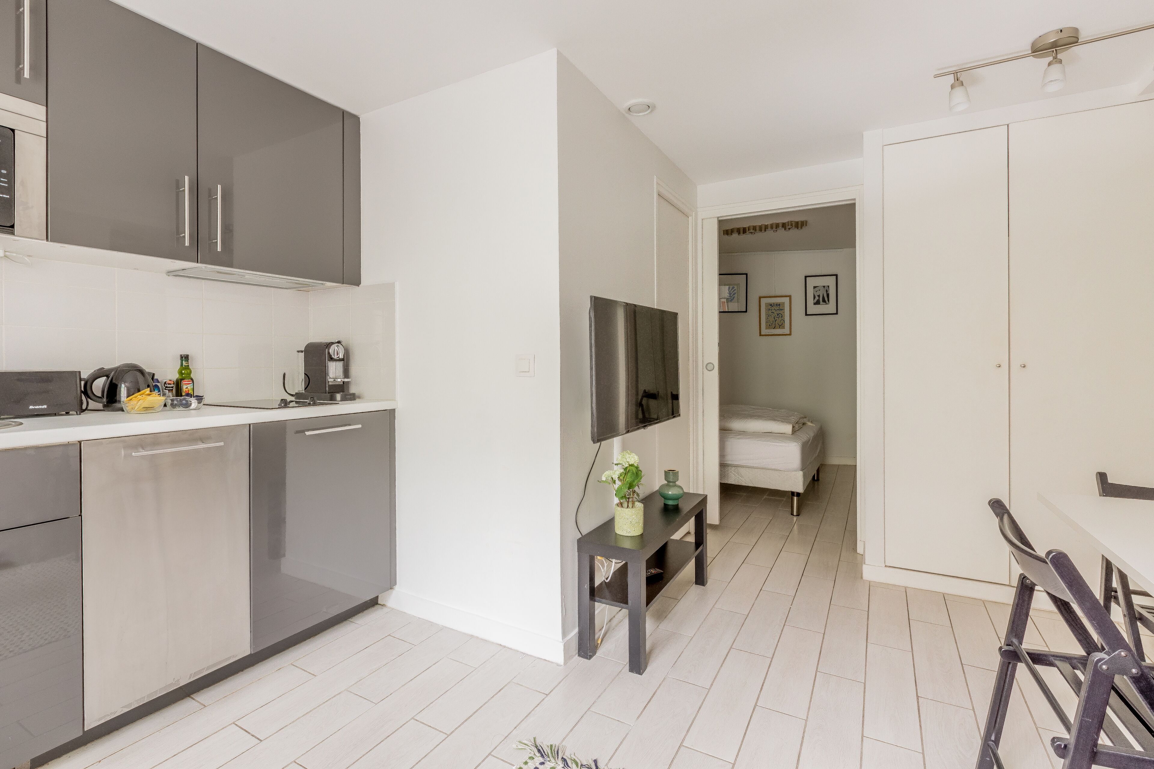 Une cuisine moderne avec des meubles gris, un coin repas avec une table et des chaises, et un petit espace détente avec un banc.
