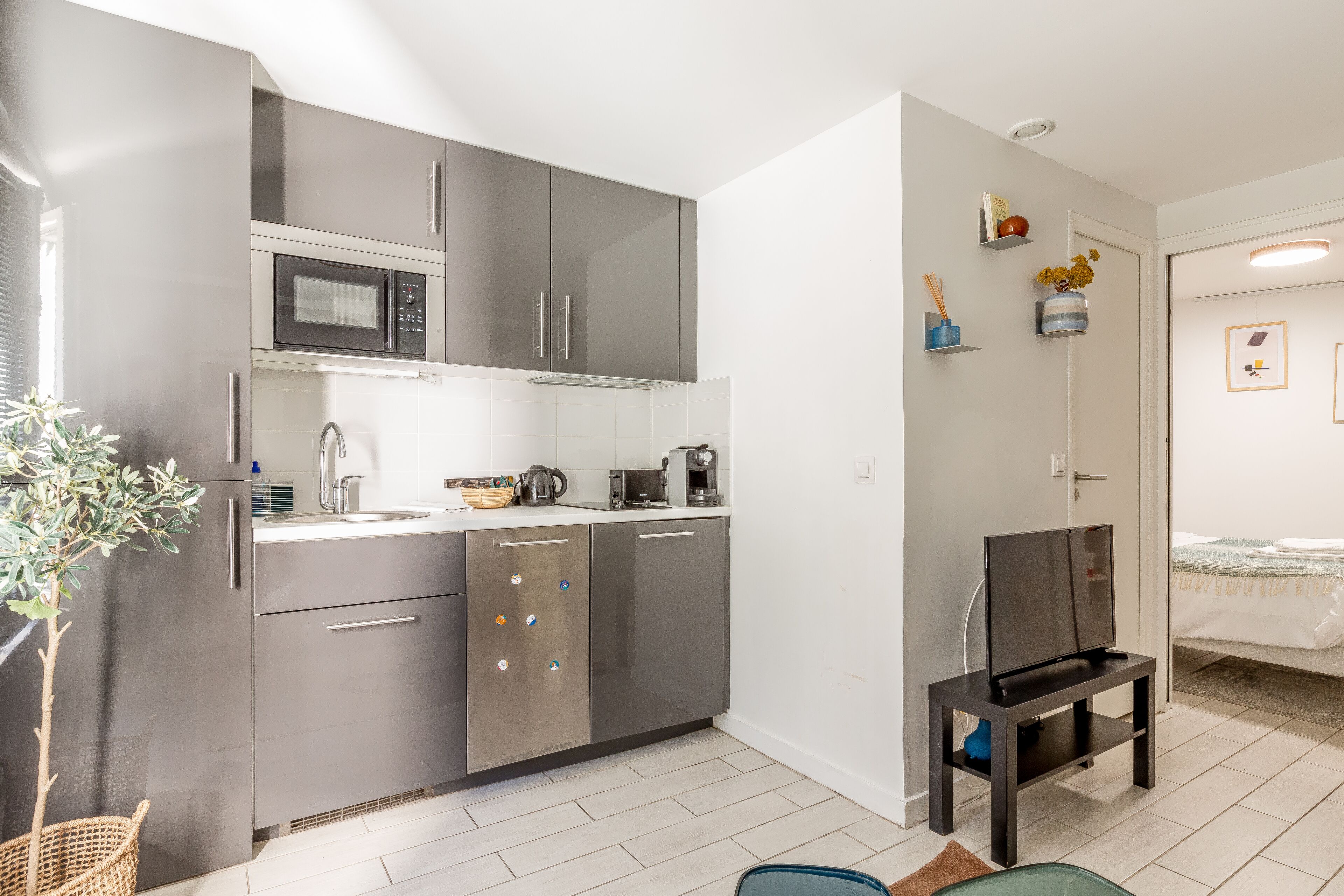 A compact kitchen with stainless steel appliances, a small dining area with a TV, and a wicker plant.
