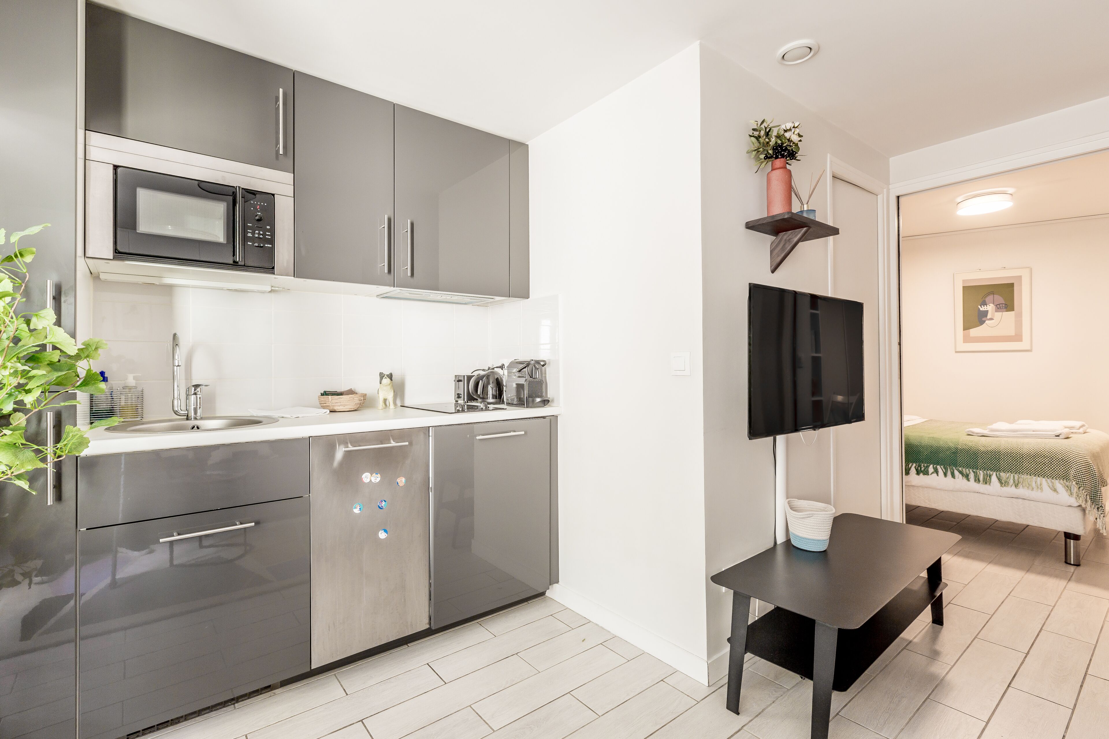 A modern kitchen with stainless steel appliances, a flat-screen TV mounted on the wall, and a small dining table.
