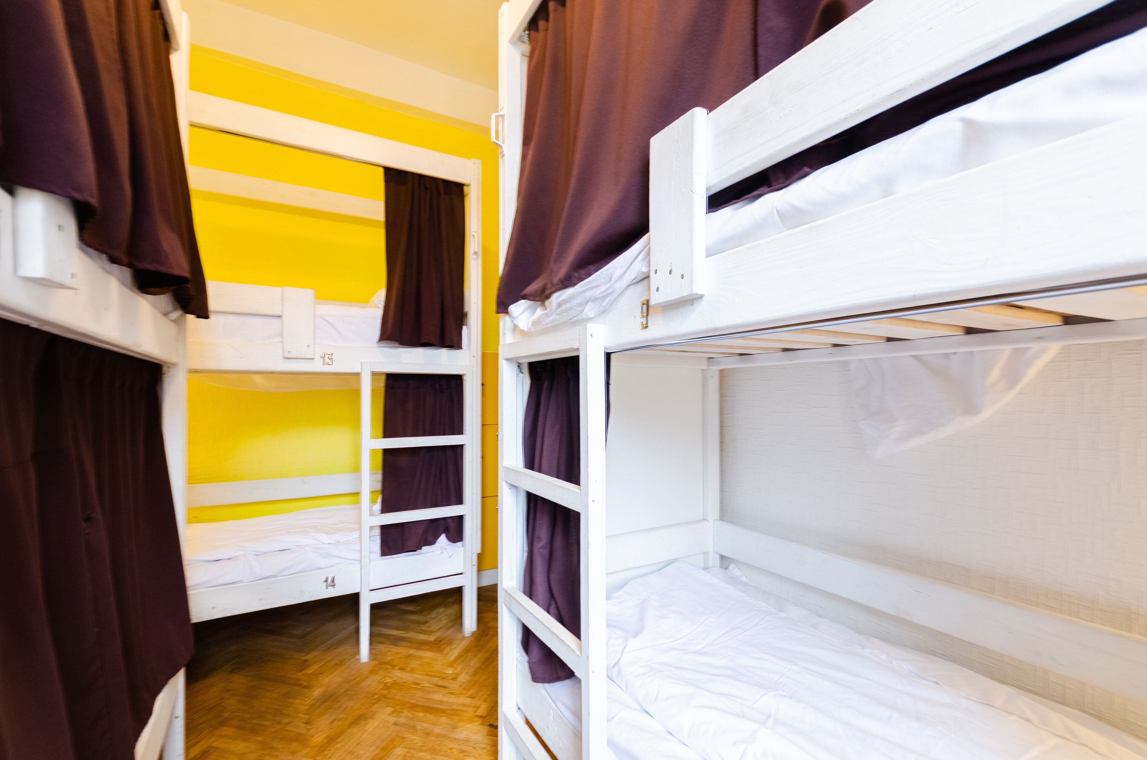 Habitación tipo dormitorio con literas, suelo de madera y pared amarilla.