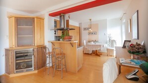 A modern kitchen with wooden cabinets, a central island, and a dining area with a white table and chairs. - Canisiusbrünnl (Rum)