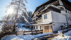 A multi-story building with a wooden facade and balconies, surrounded by snow-covered trees and a wooden fence. - Canisiusbrünnl (Rum)