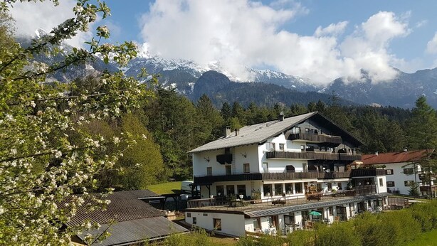 A multi-story building with balconies, surrounded by greenery and mountains in the background. - Canisiusbrünnl (Rum)