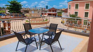 A balcony with a round table and four chairs, overlooking a cityscape with buildings and a clear sky. - Eden Hotel And Resorts (Ota)