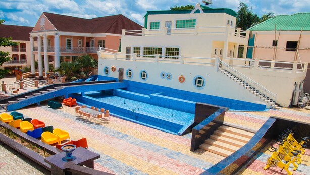 A swimming pool area with multiple levels, a covered seating area with colorful chairs, and a staircase leading to an upper deck. - Eden Hotel And Resorts (Ota)