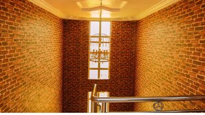 A narrow stairwell with brick walls, a metal handrail, and a large window with a decorative grille. - Eden Hotel And Resorts (Ota)