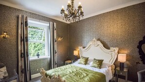 A bedroom with a large bed, ornate headboard, and a chandelier. - The Elmfield (Ilfracombe)