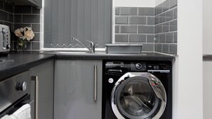 A compact kitchen with grey cabinets, a built-in dishwasher, and a grey tiled backsplash. - Burton House (Leeds)