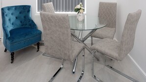 A modern living room with a glass coffee table, two chairs, a blue armchair, and a window with blinds. - Burton House (Leeds)