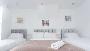 A hotel room with a large bed, two smaller beds, and a headboard with a tufted design. - Burton House (Leeds)