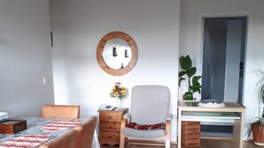 Ein gemütliches Wohnzimmer mit Esstisch, bequemen Stuhl, kleinem Schreibtisch und einem großen Spiegel an der Wand.