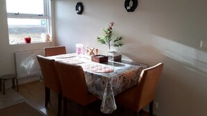 Ein Essbereich mit Tisch für vier Personen, ausgestattet mit einer blumigen Tischdecke, Stühlen, einer Blumenvase und einer mit „TEE“ beschrifteten Schachtel.