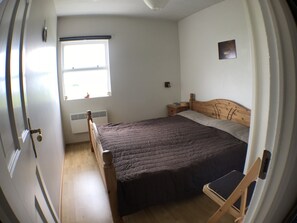Un dormitorio con una cama de madera, una ventana con persianas, una mesita de noche y un tocador.