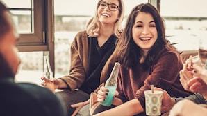 Un grupo de personas sentadas en el interior, sosteniendo bebidas y conversando.