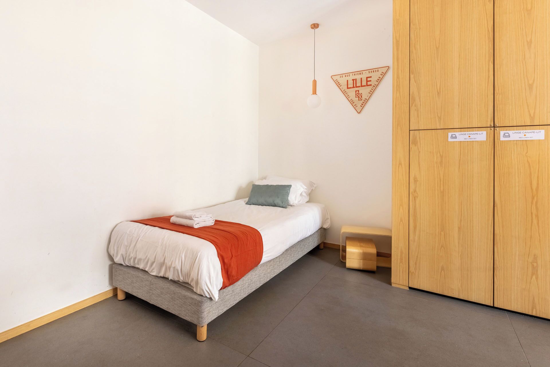 Een compacte, netjes ingerichte slaapkamer met een enkel bed, een houten garderobe en een klein nachtkastje.