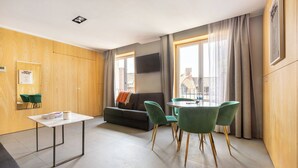 A modern room with a sofa, a dining table with chairs, a TV mounted on the wall, and a window with curtains. - Au Chat Qui Dort Lille - Thiers (Lille)
