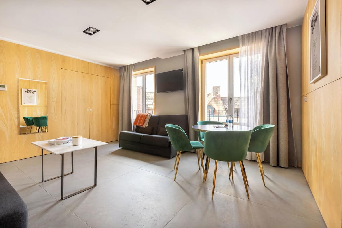 A modern room with a sofa, a dining table with chairs, a TV mounted on the wall, and a window with curtains.