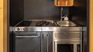 A compact kitchen with a gas stove, a built-in oven, a microwave, and wooden shelves with kitchenware. - Au Chat Qui Dort Lille - Thiers (Lille)