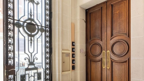 A double wooden door with a brass handle, a glass panel with a decorative metal frame, and a green emergency exit sign above. - Au Chat Qui Dort Lille - Thiers (Lille)
