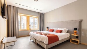 A modern hotel room with a large bed, a bedside table, a lamp, and a view of the city through the window. - Au Chat Qui Dort Lille - Thiers (Lille)