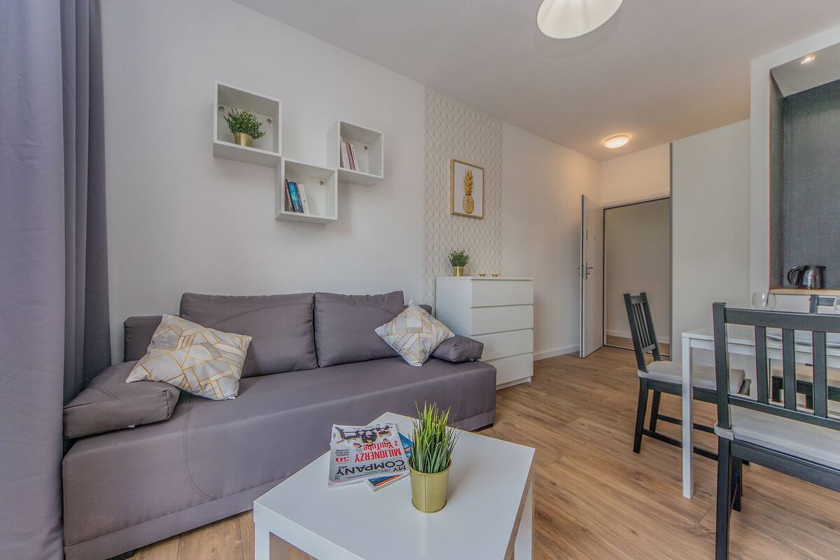 Un salon moderne avec un canapé gris, une table basse blanche et une petite bibliothèque.