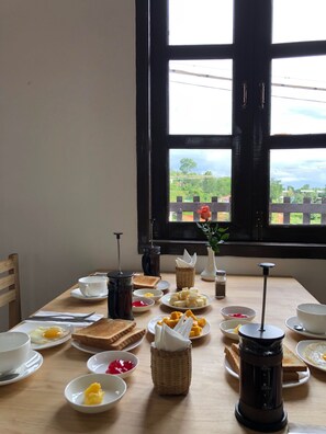 A breakfast table with various food items and a coffee press, set against a window with a view of greenery. - Hinode Hotel (Kalaw)