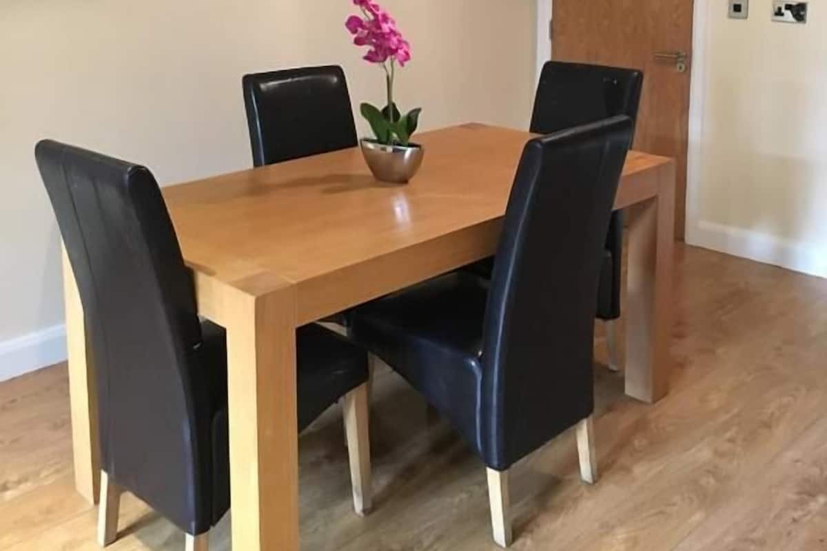 A dining area with a wooden table and black chairs, a potted plant, and a pendant light.