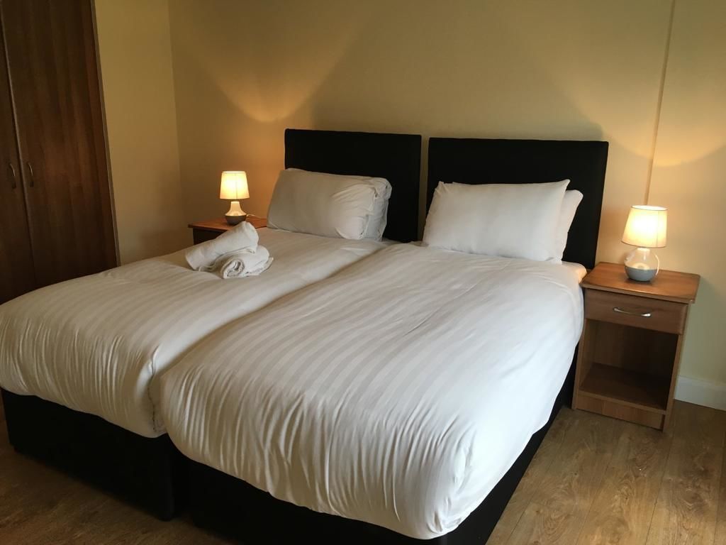 A neatly made bed with white linens, two bedside tables with lamps, and a wooden floor.