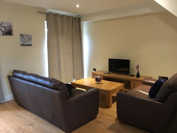 Una sala de estar con un sofá de cuero marrón, una mesa de centro de madera y un televisor de pantalla plana sobre un mueble de madera.