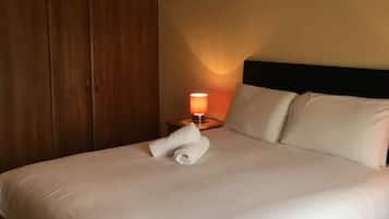 Una cama bien hecha con sábanas blancas, una toalla enrollada, una lámpara de noche y un armario de madera en una habitación de hotel.