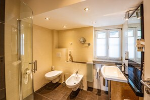Features a glass-enclosed shower, separate bidet, and vanity with sink and mirror.